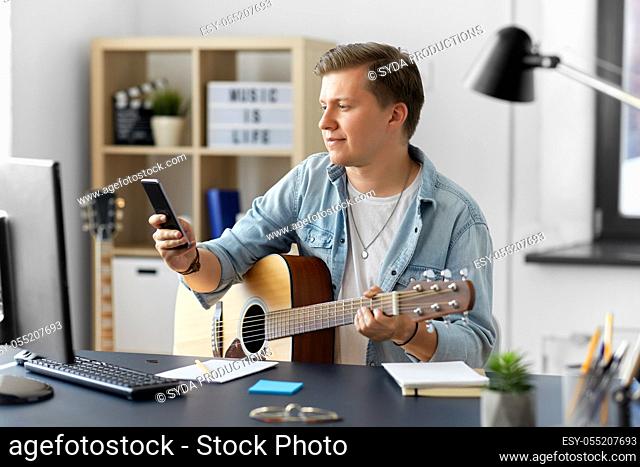 young man with guitar and smartphone at home
