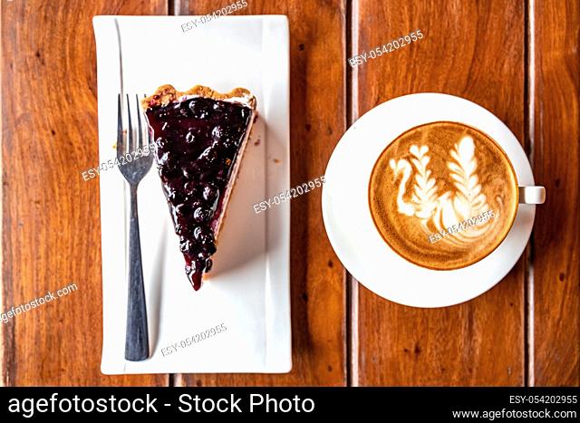 Top view of coffee and blueberry cheesecake placed on a wooden surface