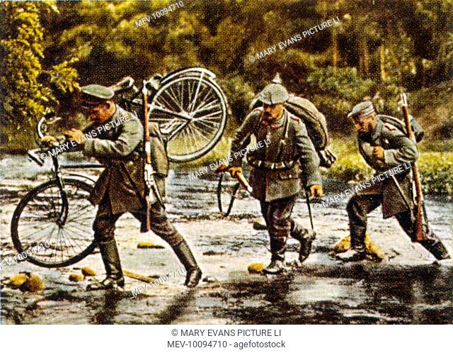 German troops, one carrying his bicycle, cross a stream as they move into Eastern France