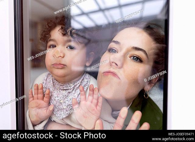 Mother and daughter looking through window pressing faces on glass pane