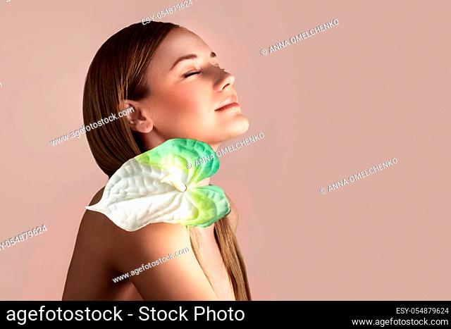 Portrait of a gentle woman with calla flower isolated on beige pink pastel background, genuine beauty, conceptual photo of a spa therapy and skin care