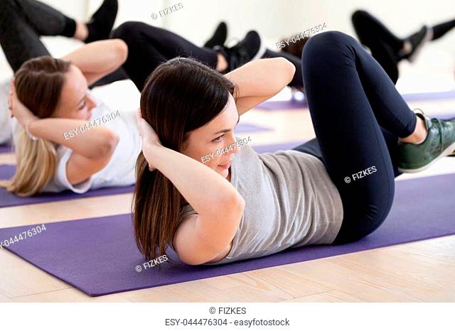 Attractive woman and group of young sporty people practicing in sport gym, doing crisscross pose, bicycle crunches exercise, working out, indoor full length