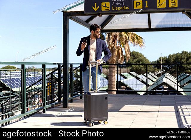 Businessman with smartphone and trolley bag standing on roof terrace of an airport