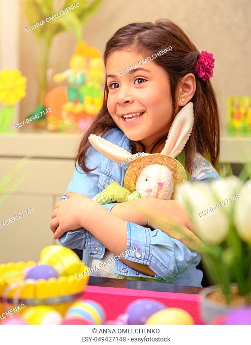 Portrait of adorable little girl with pleasure hugging her friend, soft toy Easter bunny, having fun at home in happy holiday day