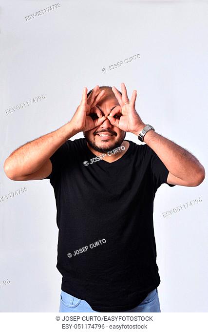 latin american man looking through fingers as if wearing glasses on white background