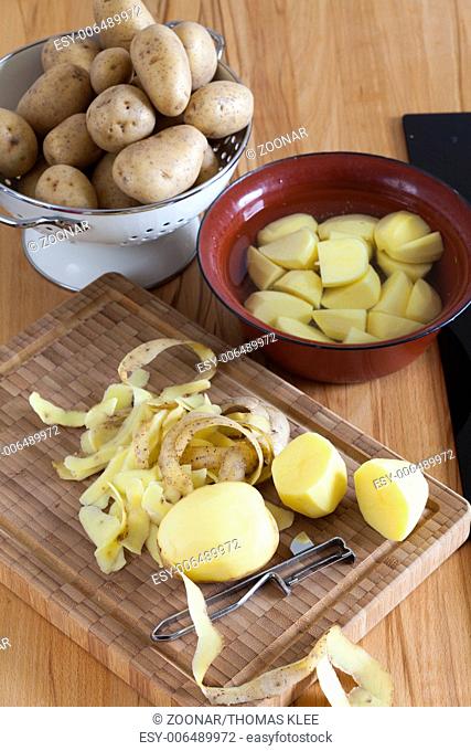 Raw potatoes and kitchen utensils on the worktop