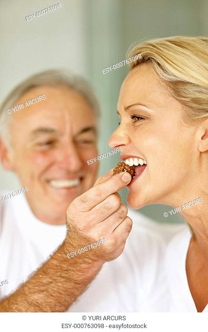Closeup of a happy husband feeding his mature wife with a piece of chocolate