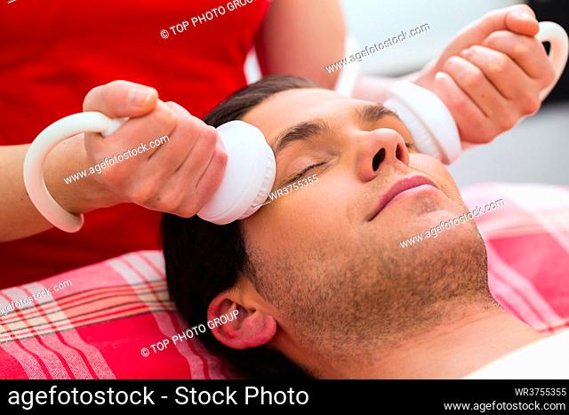 Man having relaxing herbal bag face massage in wellness spa