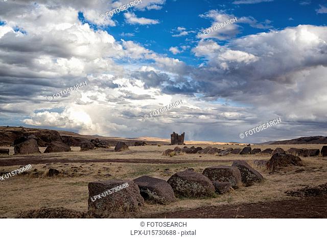 Lake Titicaca: Sillustani funerary towers with large stones leading across grassy landscape, dramatic storm clouds and light, Peru