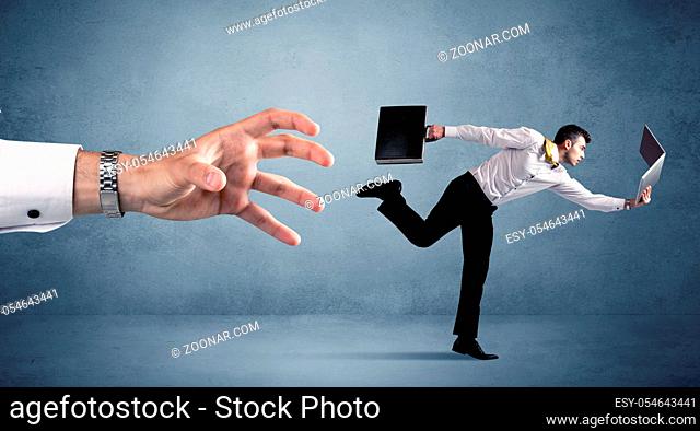 Young miniature businessman running from a big hand