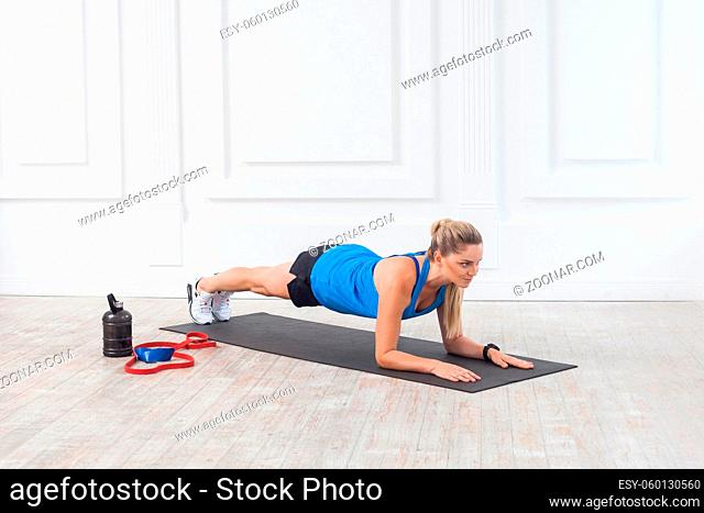 Side view of muscular sporty strong young athletic beautiful caucasian woman in black shorts and blue top standing on perfect elbow plank position