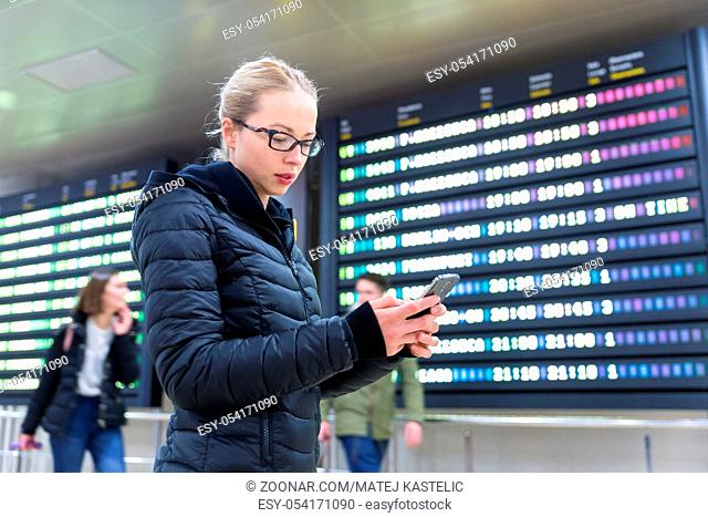 Woman in international airport looking at smart phone app information and flight information board, checking her flight detailes