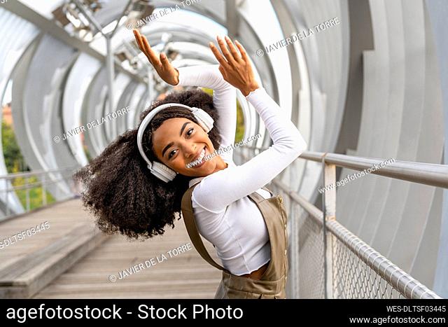 Happy woman enjoying listening to music through headphones on footbridge