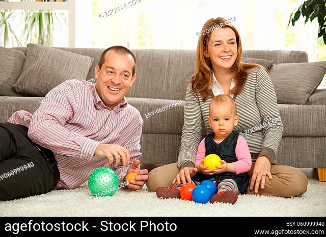 Happy smiling parents sitting with baby girl holding ball in hands at home
