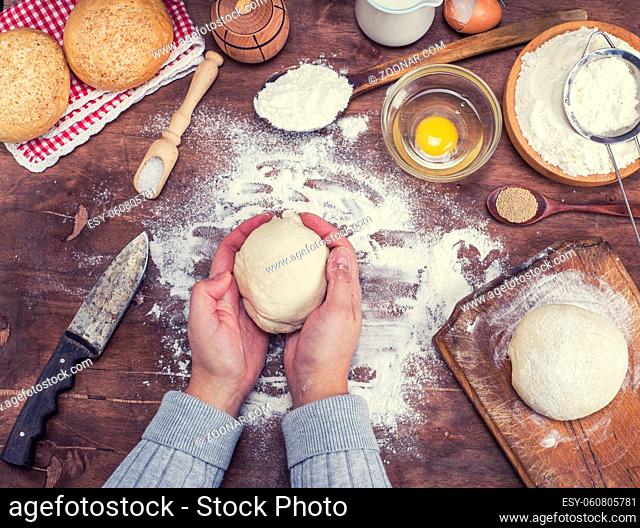 women's hands hold a ball of yeast dough on a table in the middle of the ingredients for bread making