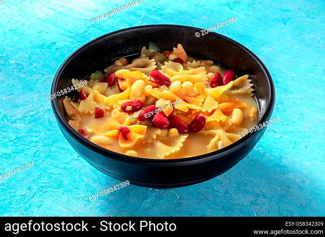 Vegan soup with vegetables, pasta and beans, on a blue background