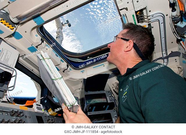 NASA astronaut Stephen Robinson, STS-130 mission specialist, looks through an overhead window on the aft flight deck of space shuttle Endeavour during flight...