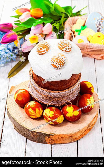 Top view traditional Easter bread covered with sugar glaze and cookies in egg shape, tulip bouquet on background, blured