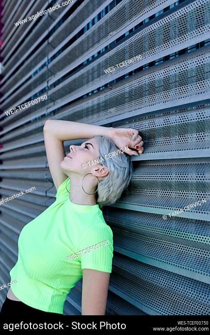 Blond woman leaning on metal background, daydreaming