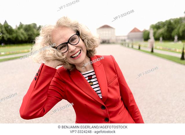 happy senior woman (67 years old) in park at touristic sight Nymphenburg palace, in Munich, Germany