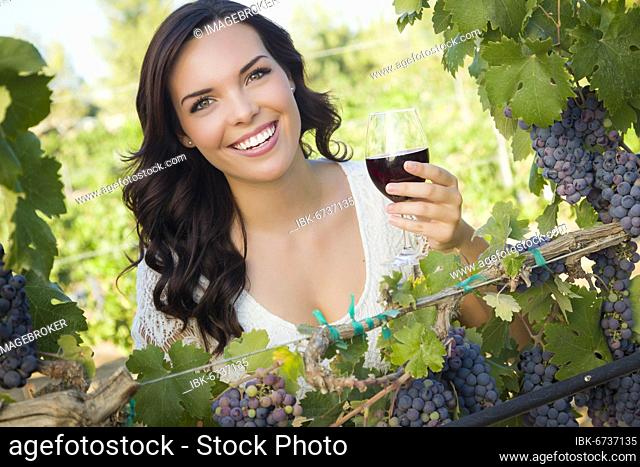 Pretty mixed race young adult woman enjoying A glass of wine in the vineyard