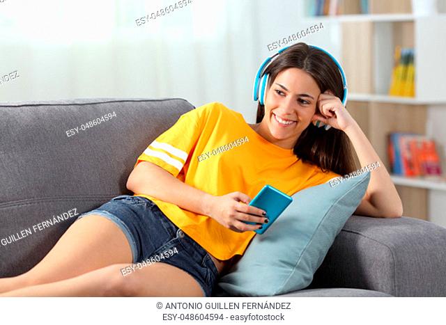 Happy teen in yellow listening to music sitting on a couch in the living room at home