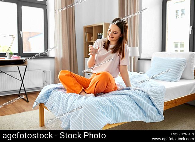 girl with glass of water sitting on bed at home