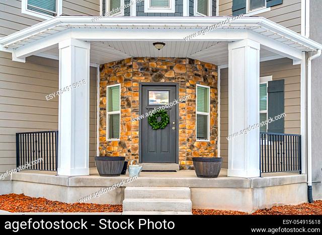 Facade of a beautiful home with a half hexagon shaped porch and wall. A wreath hangs on the glass paned front door with vertical sliding windows on both sides