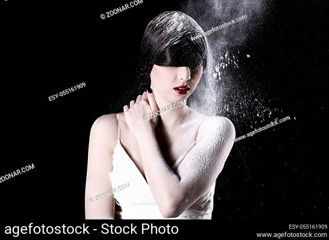 Beautiful girl in white dress and flying dust over black background