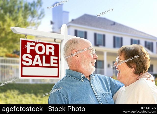 Happy senior couple front of for sale real estate sign and house