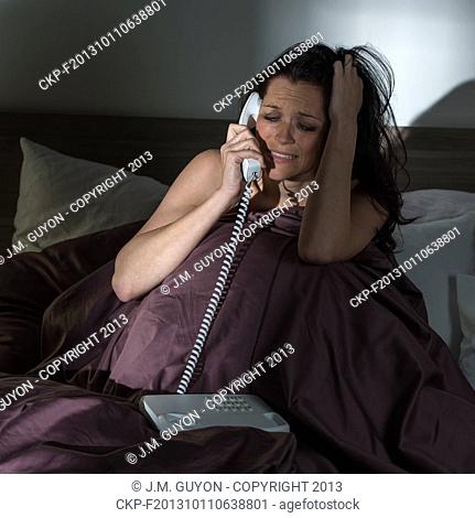 Crying young woman calling phone in bed