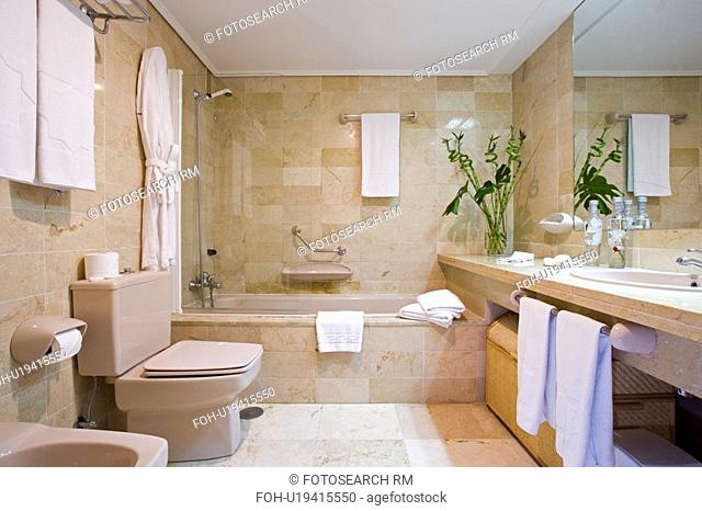 Neutral modern bathroom with marble tiled walls and floor and white towels and bathrobes