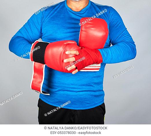 athlete in blue clothes, hands are rewound with red textile bandage, he is wearing leather sports boxing gloves, gray background