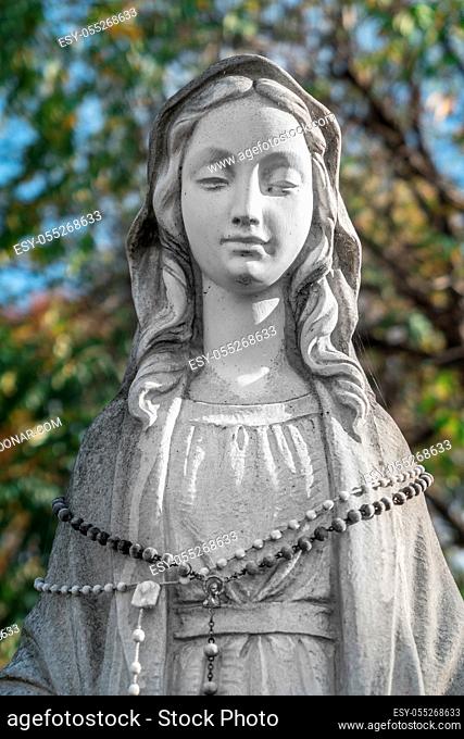 Virgin Mary Statue. On defocused blurry background some green trees. Ideal for concepts and festivity