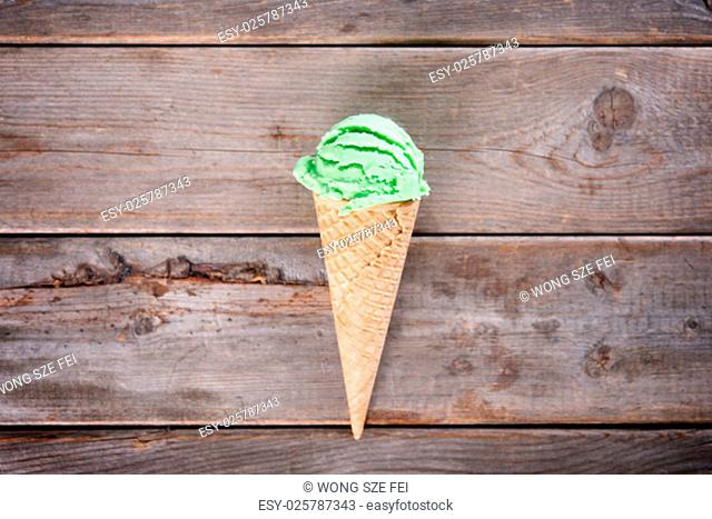 Single green tea ice cream in a waffle cone over old rustic wooden vintage background with copy space