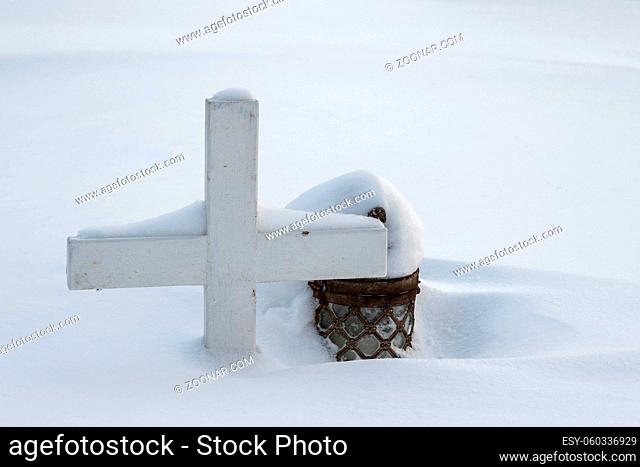 Graveyard in winter, a small wooden cross and a lantern covered in snow. Norway