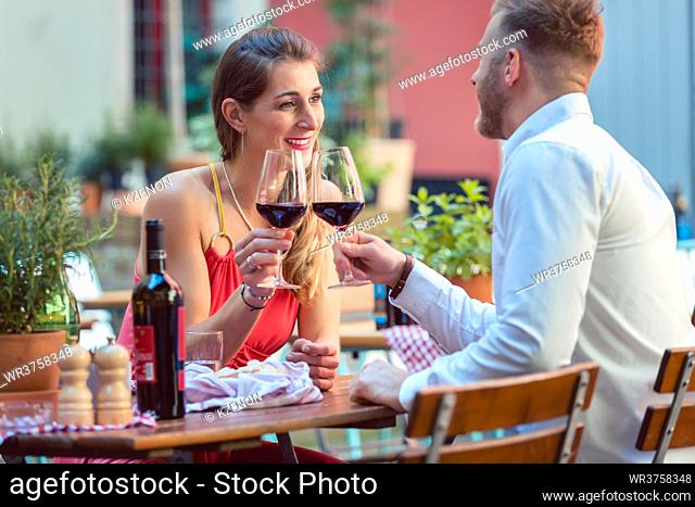 Portrait of a happy couple at restaurant toasting glass of red wine