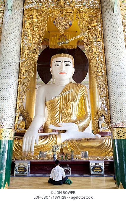 Myanmar, Yangon, Yangon. A man praying to large seated Buddha at the Shwedagon Pagoda in Yangon in Myanmar