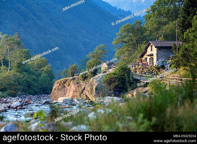 Europe, Switzerland, Ticino, Brione. Two women sit in the small plain of Brione in front of typical, idyllic Verzasca house