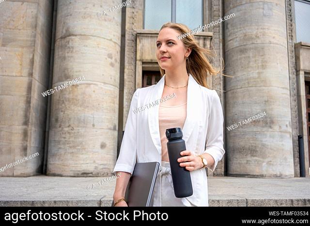 Thoughtful young businesswoman with laptop and reusable water bottle