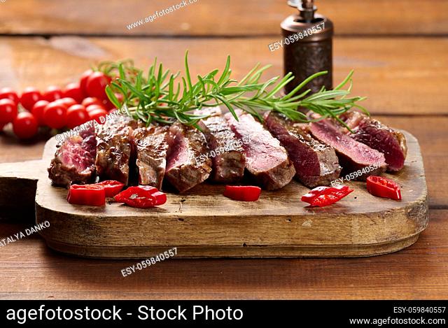 roasted piece of beef ribeye cut into pieces on a vintage brown chopping board. Well done. Appetizing steak