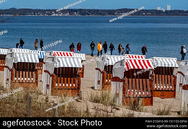 10 April 2021, Schleswig-Holstein, Timmendorfer Strand: People walk along Timmendorfer Strand in bright sunshine behind the first beach chairs set up this year