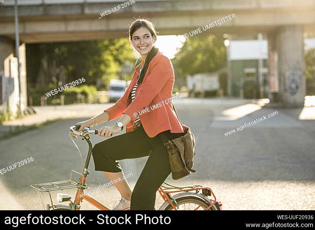 Smiling young woman riding bicycle on street in city