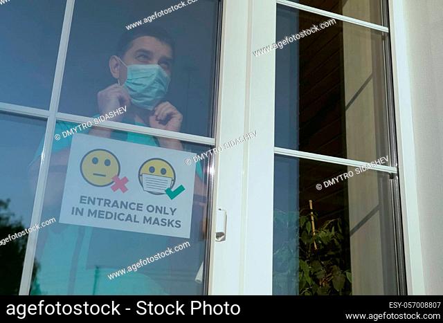 Store employee attaches the sign ENTRANCE ONLY IN MEDICAL MASKS. Small business owner comes up to the window, glues a warning sign about the obligatory wearing...