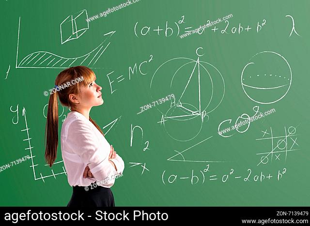 Scoolgirl standing in the classroom near a green blackboard