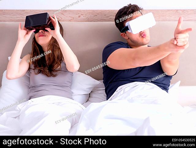The wife and husband with virtual reality goggles in the bed