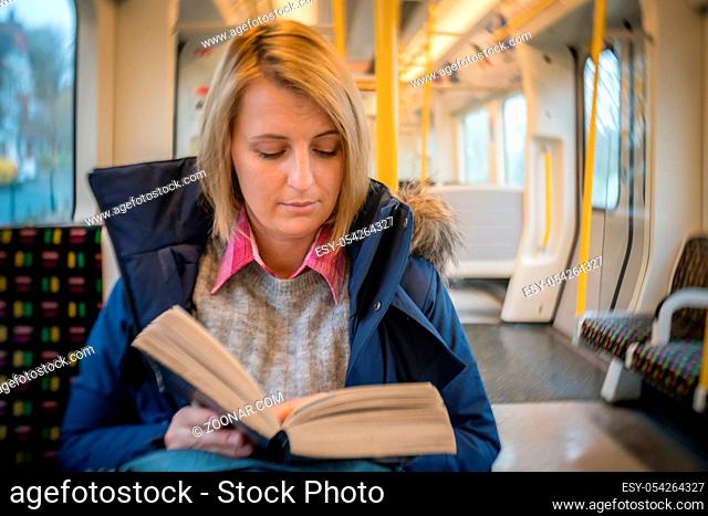 Blond Caucasian woman reading book while commuting to work in London