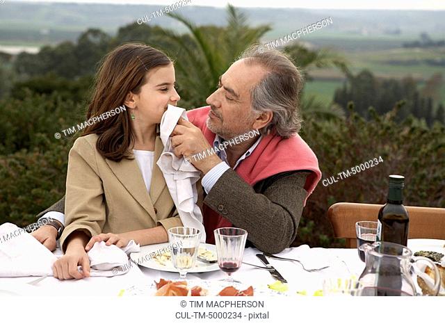 Girl 9-11 sitting with grandfather at a table outside
