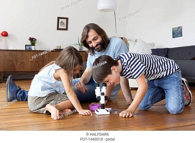 Happy family looking at boy using microscope on hardwood floor