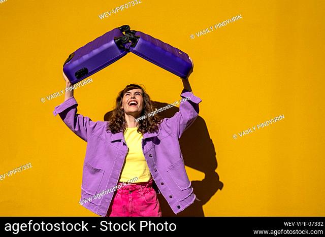 Happy woman holding open luggage in front of yellow wall